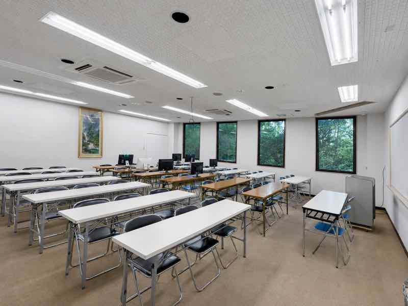 パソコンとホワイトボードを備えた、緑が見える明るい大教室